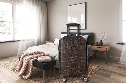 Hartschalenkoffer in brauner Krokoleder-Optik in einem stilvollen Schlafzimmer mit Bett, Nachttischen und hellen Naturtönen. Die detailreiche Reptilienstruktur verleiht dem Reisekoffer eine elegante und hochwertige Ausstrahlung für Reisen mit Stil.