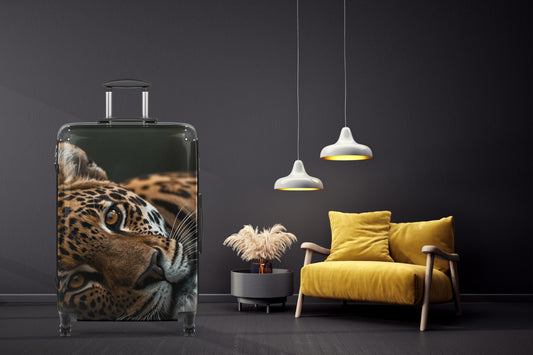 Hartschalenkoffer mit ausdrucksstarkem Leopardenmotiv in einem eleganten Wohnambiente mit dunkler Wand, warmem Licht und modernem gelbem Sessel. Die detailreiche Tierdarstellung und der intensive Blick des Leoparden verleihen dem Reisekoffer eine kraftvolle und stilvolle Ausstrahlung.