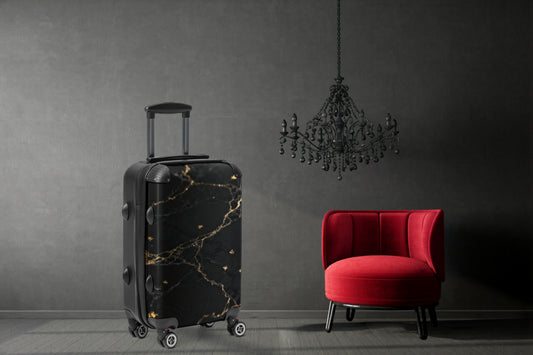 Hartschalenkoffer in schwarzer Marmoroptik mit goldenen Adern in einem eleganten Interieur mit rotem Samtsessel und dunklem Kronleuchter. Die kontrastreiche Steinstruktur und die feinen Goldadern verleihen dem Reisekoffer eine luxuriöse und ausdrucksstarke Ausstrahlung.