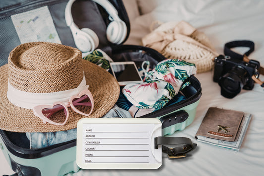 Kofferanhänger mit beschriftbarer Kontaktkarte auf der Rückseite, platziert vor geöffnetem Reisegepäck mit Sommeraccessoires und Reisezubehör.
