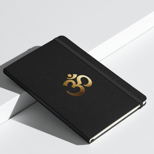 Hardcover Notizbuch mit goldenem Om-Symbol auf schwarzem Einband, stilvoll auf einer weißen Präsentationsfläche fotografiert.