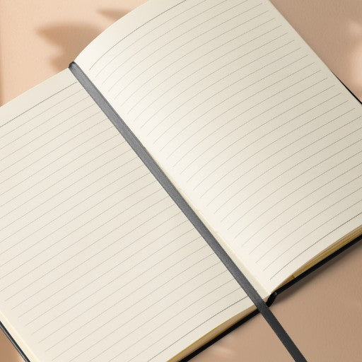Hardcover Notizbuch mit geöffneten cremefarbenen linierten Seiten und integriertem Leseband in Nahaufnahme.