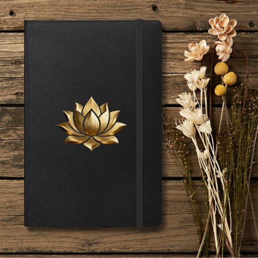 Hardcover Notizbuch mit goldener Lotusblüte auf schwarzem Einband, dekorativ auf einem Holzhintergrund mit getrockneten Blumen arrangiert.