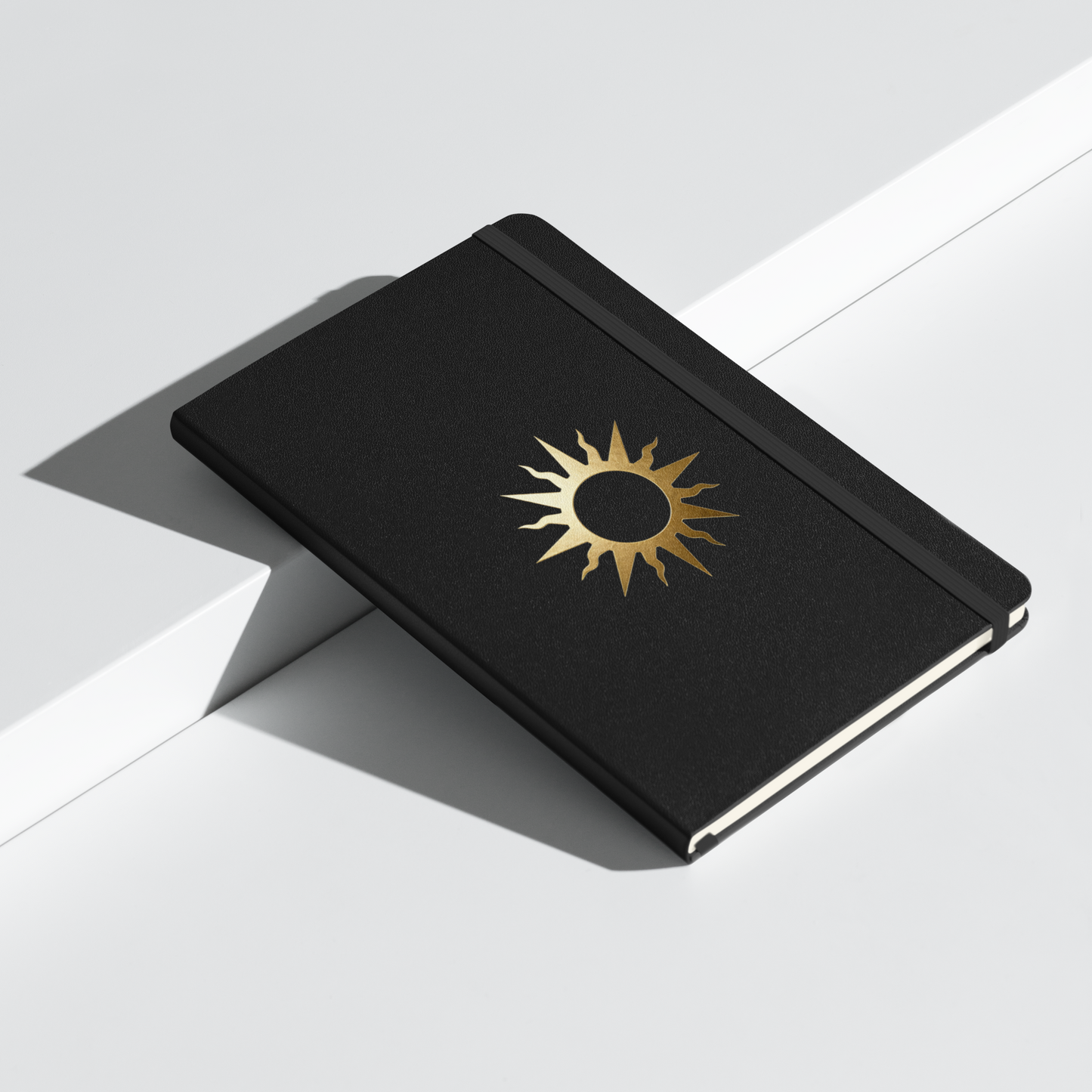 Spiralnotizbuch mit goldenem Sonnensymbol auf schwarzem Einband, dekorativ auf einem weißen Podest präsentiert.