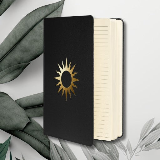 Spiralnotizbuch mit goldenem Sonnensymbol auf schwarzem Einband, geöffnet mit sichtbaren linierten cremefarbenen Seiten.
