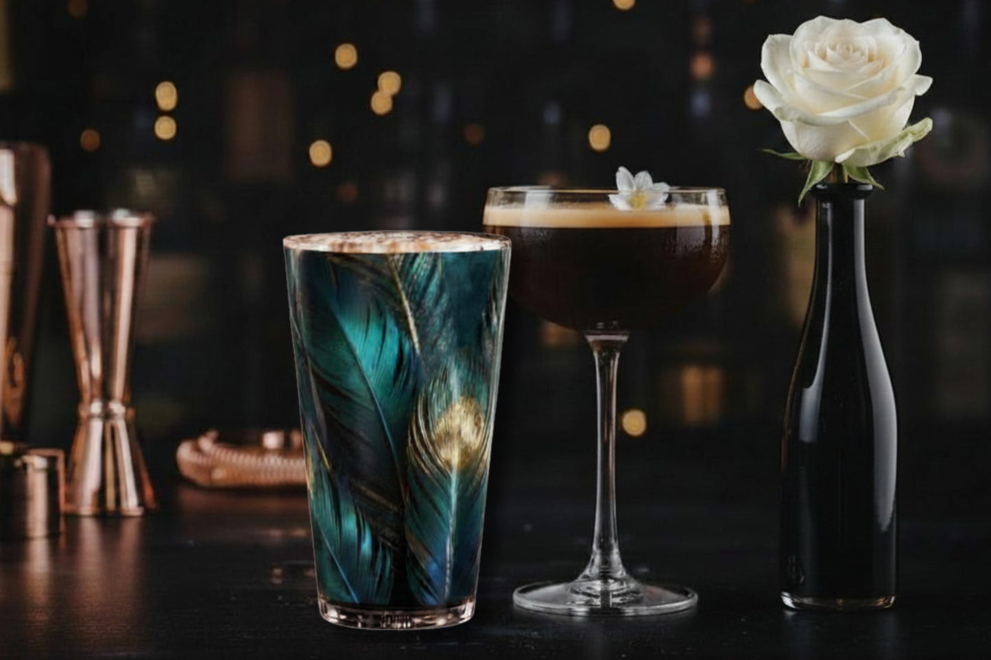 Glas mit türkis-goldenem Federmotiv in stilvoll dekorierter Bar mit weiterem Coctailglas und weißer Rose in schwarzer Vase mit stimmungsvoller Beleuchtung