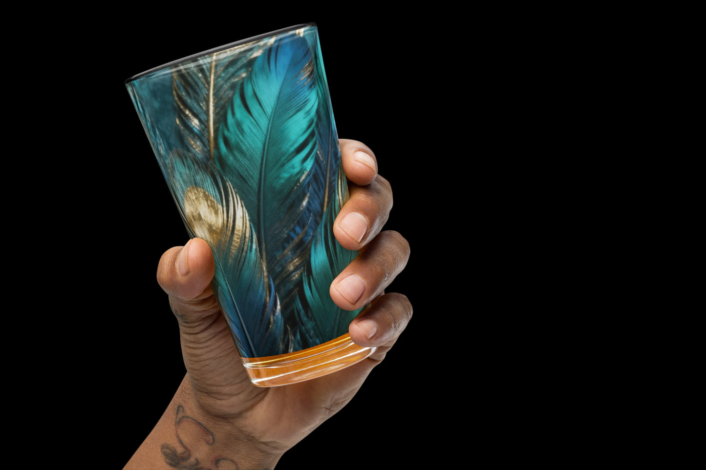 Glas mit türkis-goldenem Federmotiv in einer Hand vor schwarzem Hintergrund