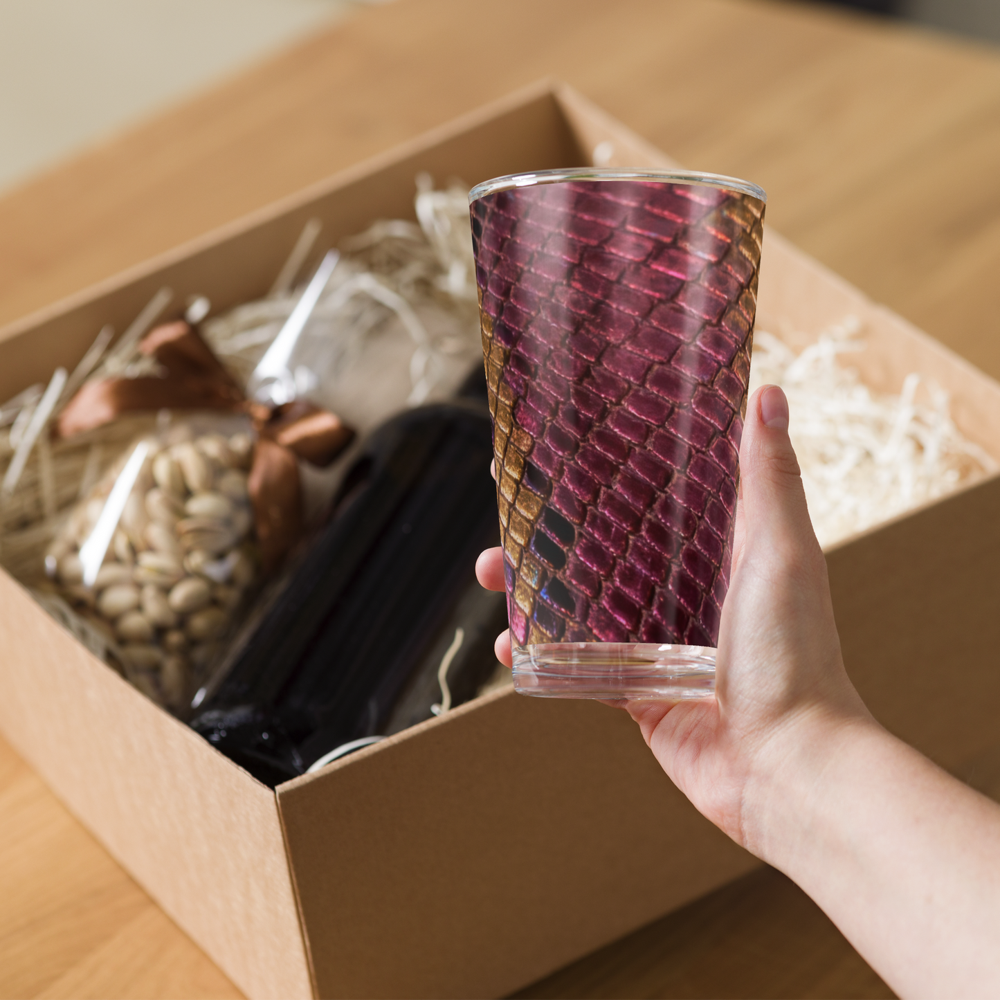 Handaufnahme der Rückseite des luxuriösen Magenta-Gold Glases mit strukturierter Reptilienoptik neben stilvoller Versandverpackung
