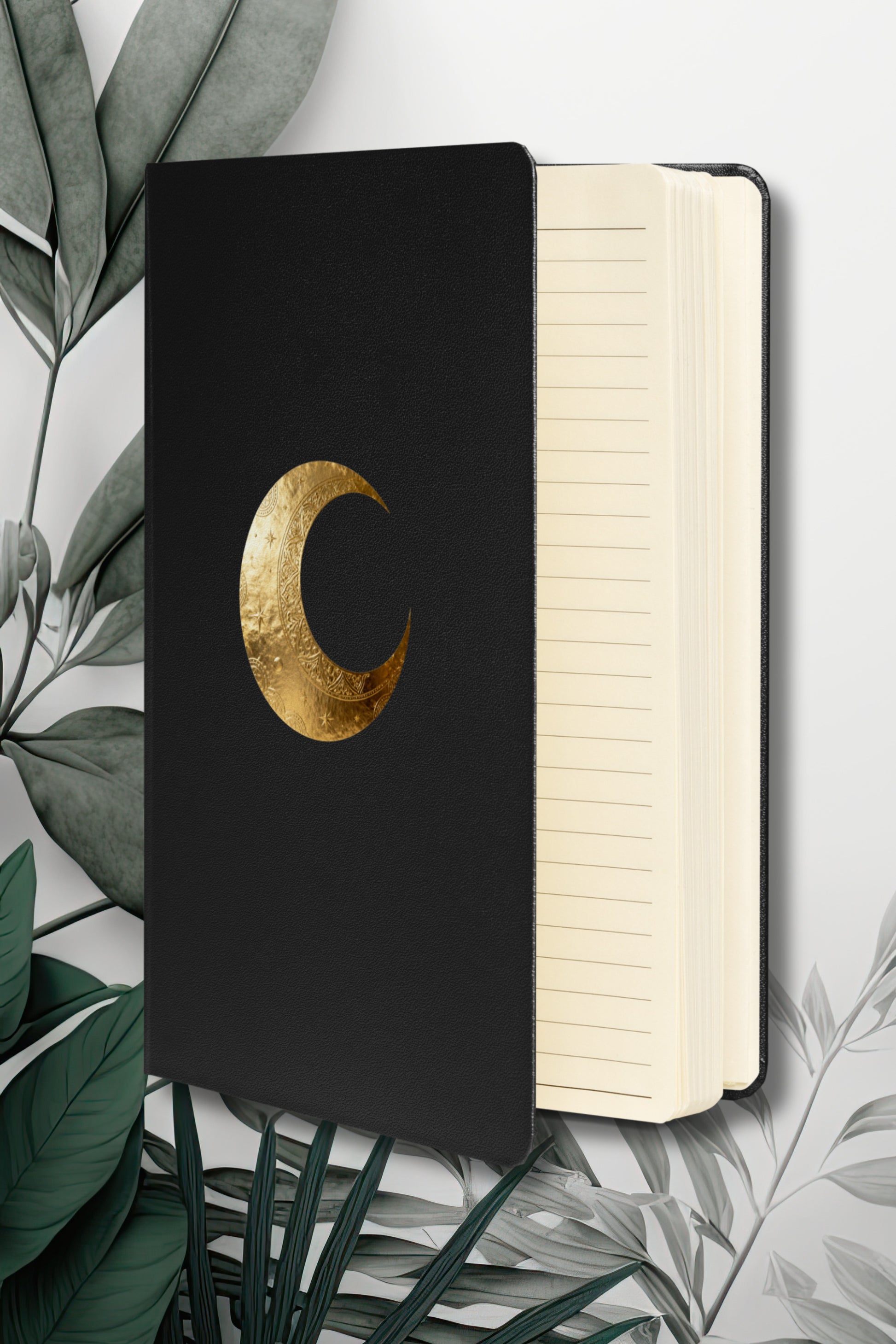Hardcover Notizbuch mit goldenem Mondsymbol auf schwarzem Einband, geöffnet mit linierten cremefarbenen Seiten.