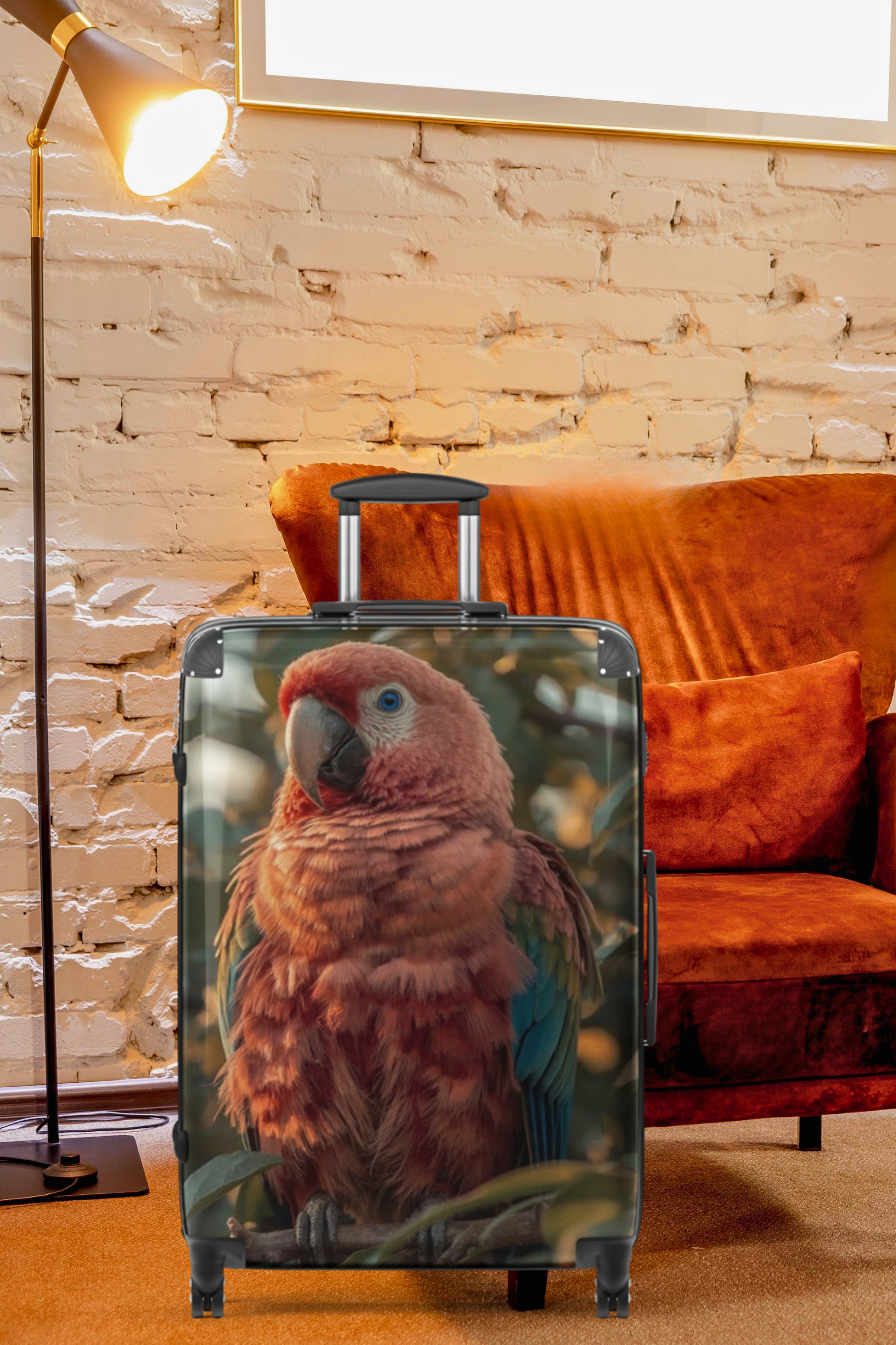 Hartschalenkoffer mit farbenprächtigem Ara-Motiv in einem gemütlichen Wohnambiente mit Ziegelwand, Stehleuchte, gemütlichem Sessel und warmen Farbtönen. Das detailreiche Vogelmotiv verleiht dem Reisekoffer eine exotische und ausdrucksstarke Ausstrahlung.