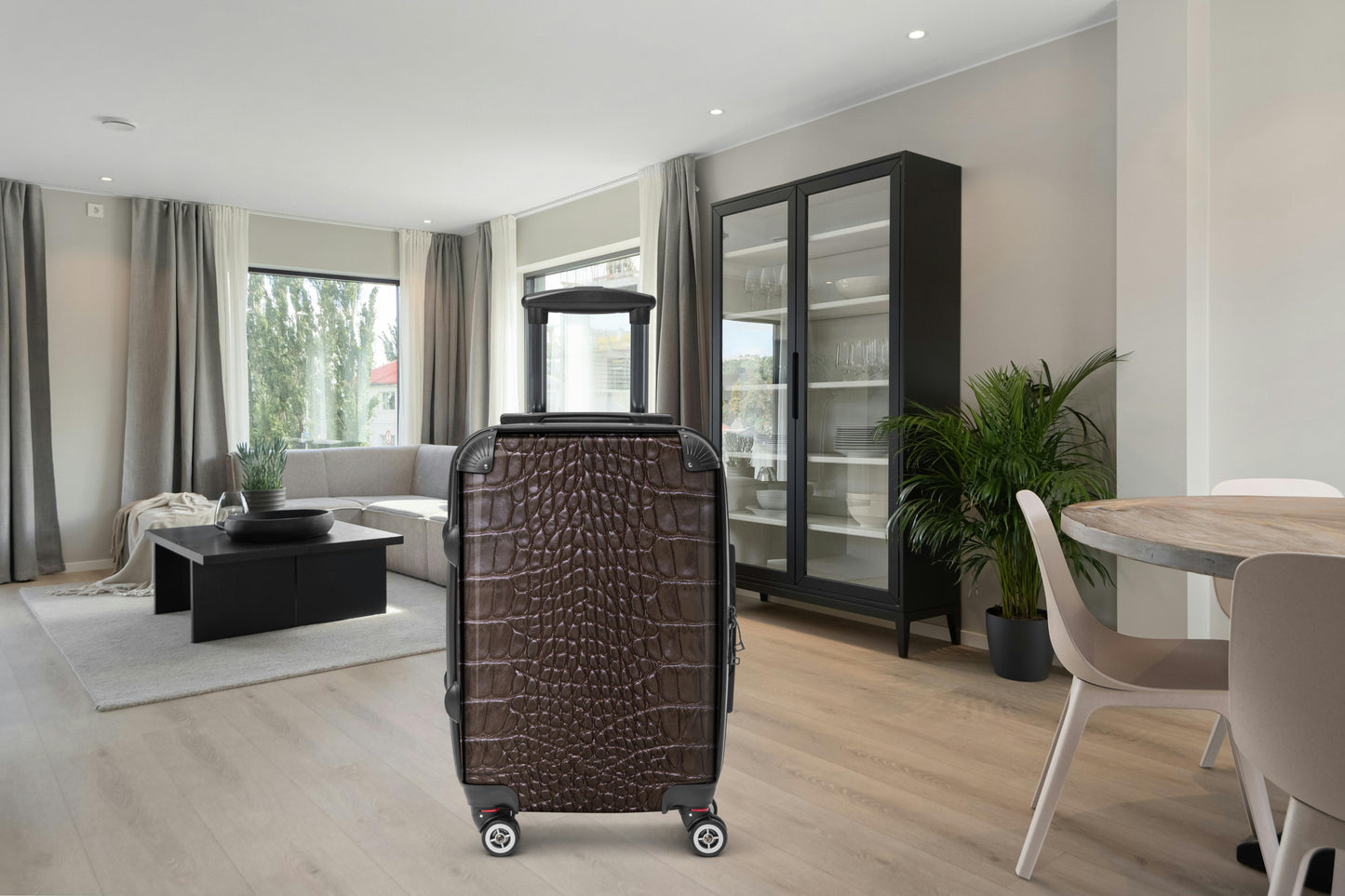 Frontalansicht eines Hartschalenkoffers in brauner Krokoleder-Optik in einem modernen Wohnbereich mit hellen Holzböden, großen Fenstern und eleganter Einrichtung. Die Aufnahme zeigt die strukturierte Kofferoberfläche, den ausziehbaren Teleskopgriff sowie die vier 360-Grad-Doppelrollen für komfortables Reisen.