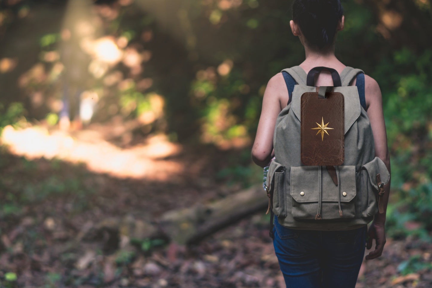 Kofferanhänger mit goldenem Polarstern auf dunkelbrauner Lederoptik, befestigt an einem Rucksack auf einem Waldpfad und umgeben von natürlicher Outdoor-Kulisse.