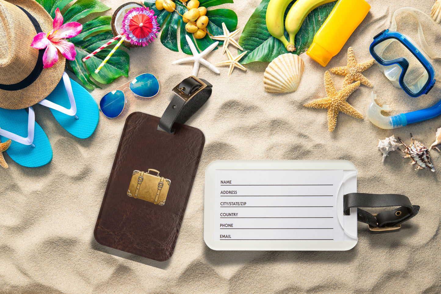 Kofferanhänger mit goldenem Reisekoffer-Motiv auf brauner Lederoptik am Strand mit geöffneter Rückseite und Kartenfach, umgeben von sommerlichen Reiseaccessoires.
