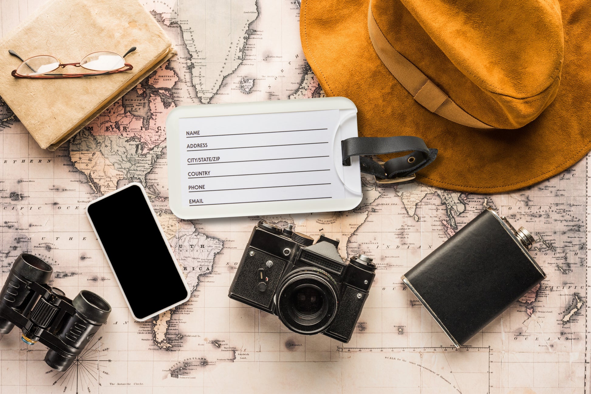 Kofferanhänger Rückseite mit integriertem Kartenfach für Kontaktdaten, Visiten- oder Kreditkarten präsentiert auf einer Weltkarte mit Reiseutensilien wie Kamera, Fernglas, Smartphone und Hut.