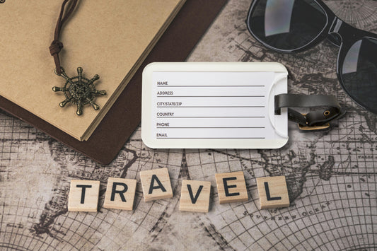 Rückseite eines Kofferanhängers mit Kartenfach für Kontaktdaten auf einer Reisekarte neben Notizbuch und Sonnenbrille