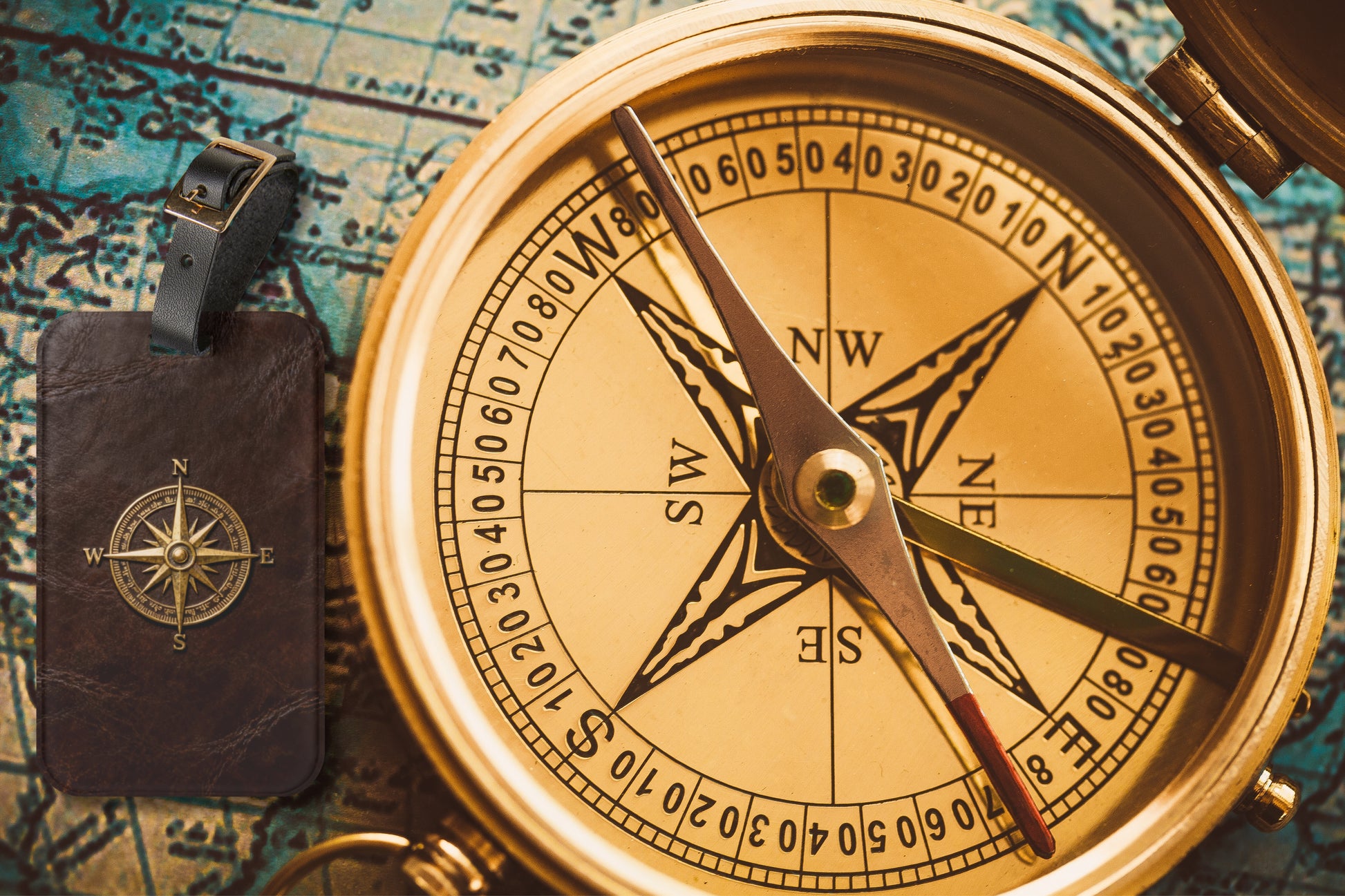 Kofferanhänger mit goldenem Vintage-Kompass auf brauner Lederoptik neben einem antiken Kompass und einer historischen Landkarte im Explorer-Stil.