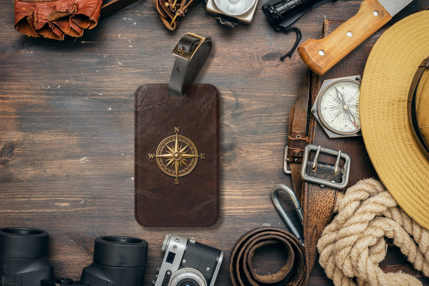 Kofferanhänger mit goldenem Vintage-Kompass auf brauner Lederoptik umgeben von klassischer Reiseausrüstung wie Kompass, Kamera, Fernglas und Hut im Explorer-Stil.