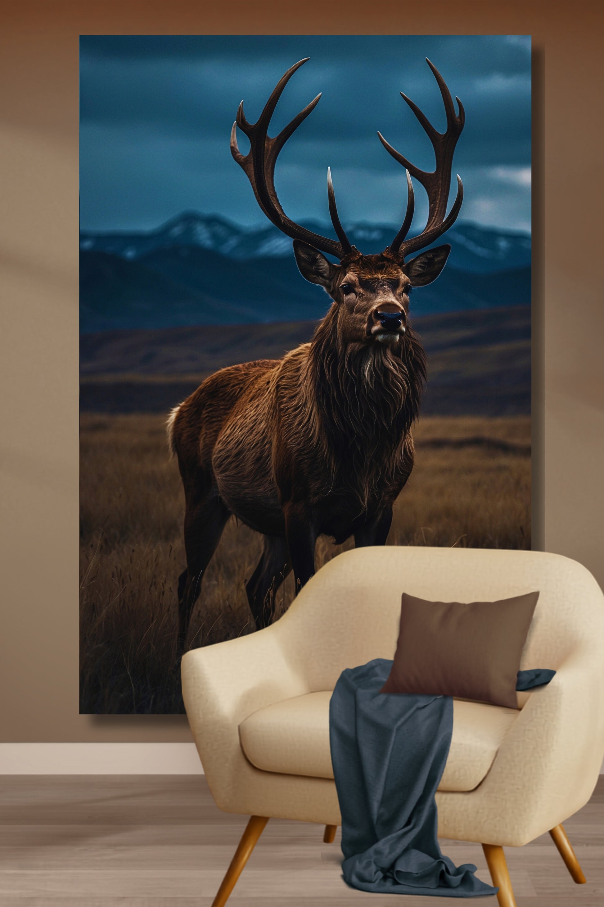 Leinwand eines Hirsches in weiter Landschaft an einer beigefarbenen Wand über einem hellen Sessel mit einer Wohndecke und einem Kissen