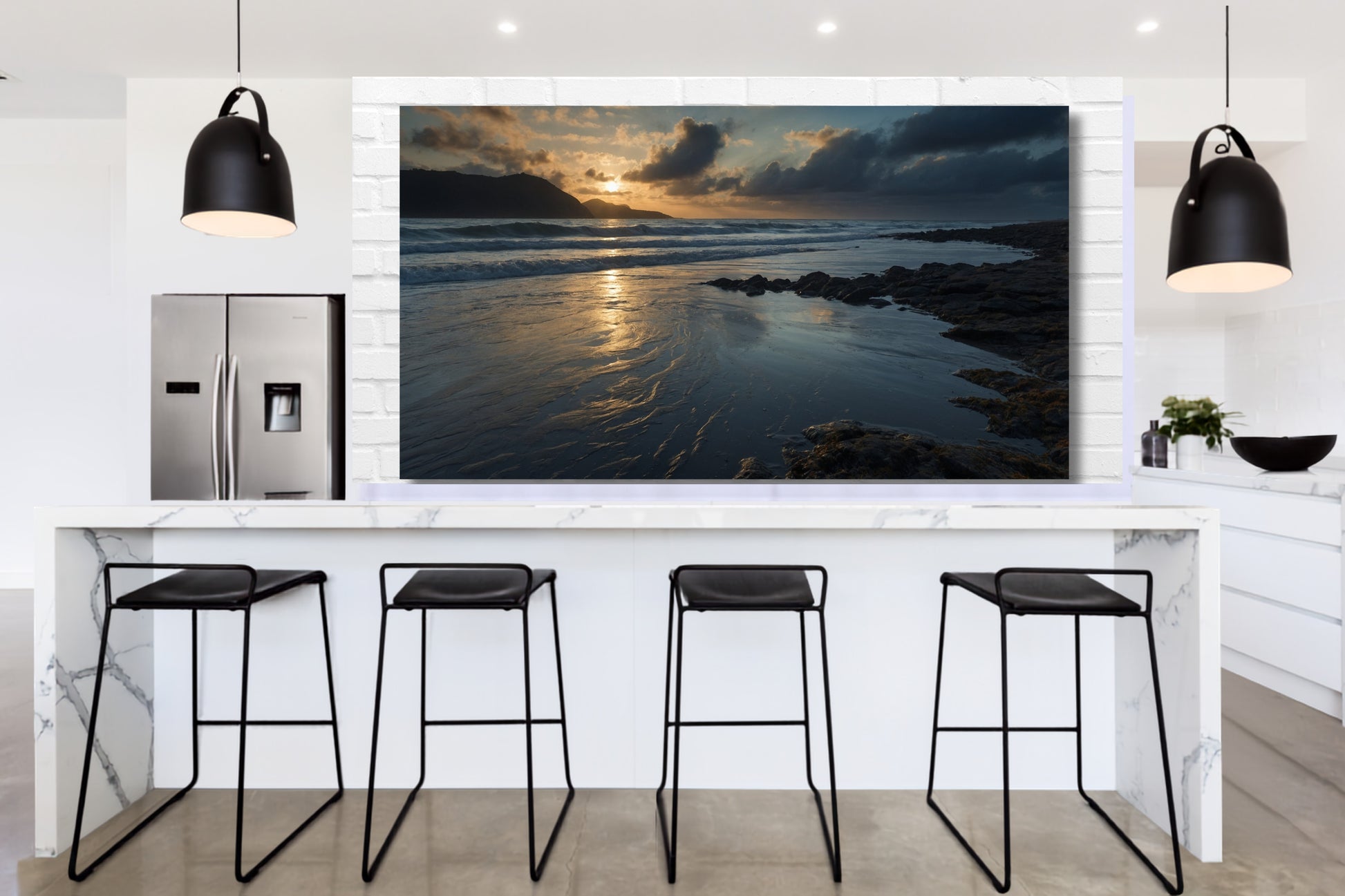 Poster einer Meereslandschaft in der Dämmerung über einer modernen Kücheninsel in einer hellen Küche mit schwarzen Pendelleuchten und Barhockern.