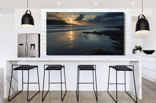 Poster einer Meereslandschaft in der Dämmerung über einer modernen Kücheninsel in einer hellen Küche mit schwarzen Pendelleuchten und Barhockern.