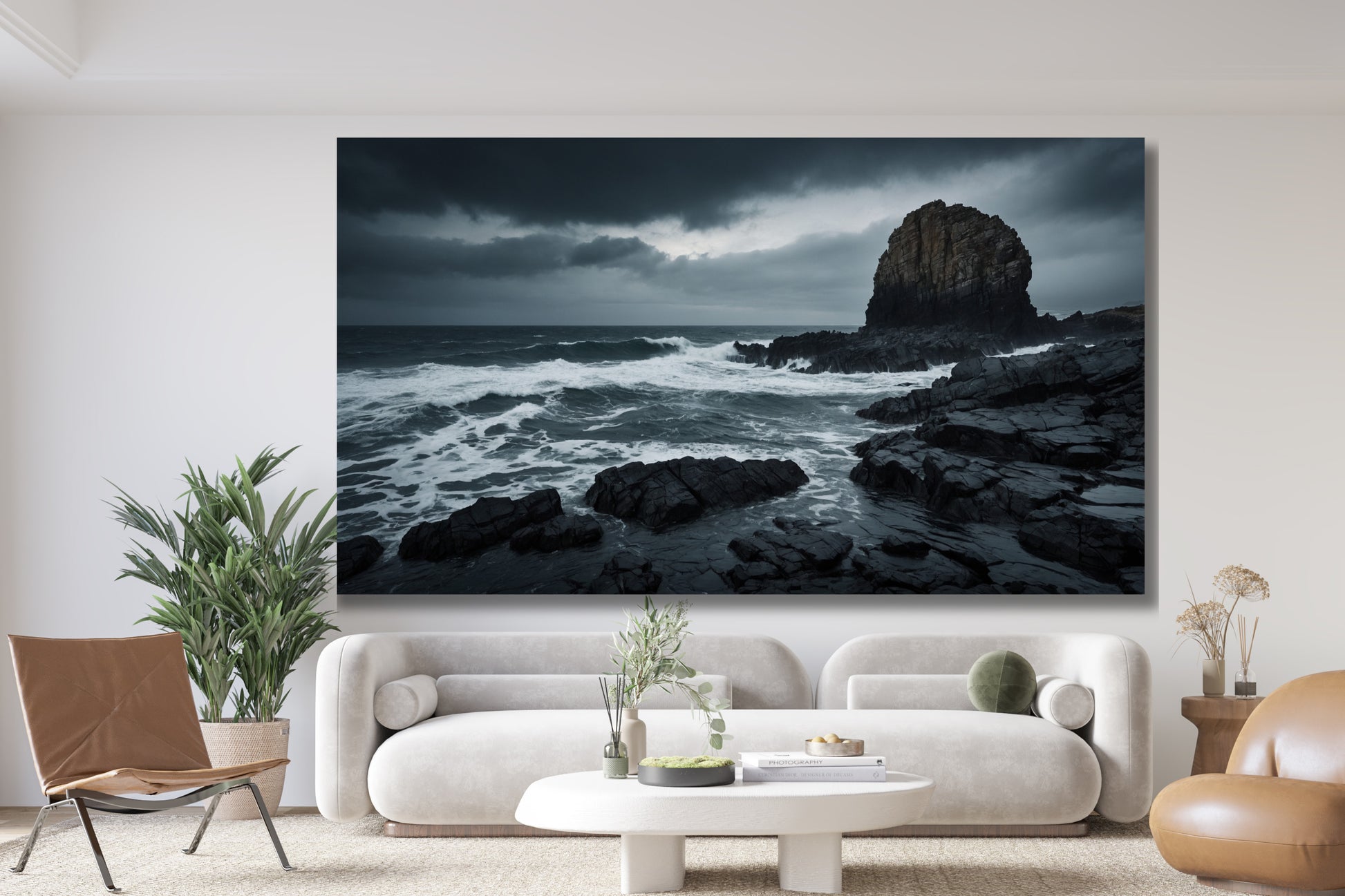 Poster einer Sturmküste mit schwarzen Felsen über einem hellen Sofa in einem modernen Wohnzimmer mit weißer Wand, Couchtisch, Zimmerpflanzen und braunem Ledersessel.
