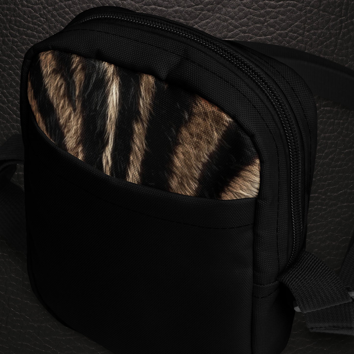 Schrägansicht der kompakten Zebra Muster Umhängetasche mit natürlichem Fellprint  schwarzem Trageriemen und Fokus auf die schwarze Aussentasche